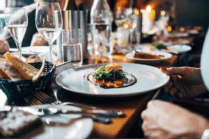 A gourmet dish with greens and sauce is served on a plate at a sophisticated dining setting with glasses and bread.
