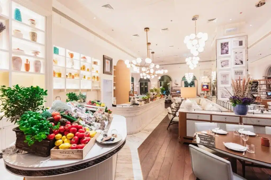 Bright, elegant GAIA Dubai restaurant interior with a fruit and herb display in the foreground and tables set for dining in the background.