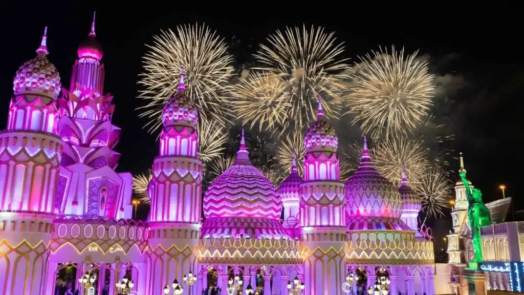 Colorful domed buildings lit in purple and pink with fireworks bursting in the night sky above.
