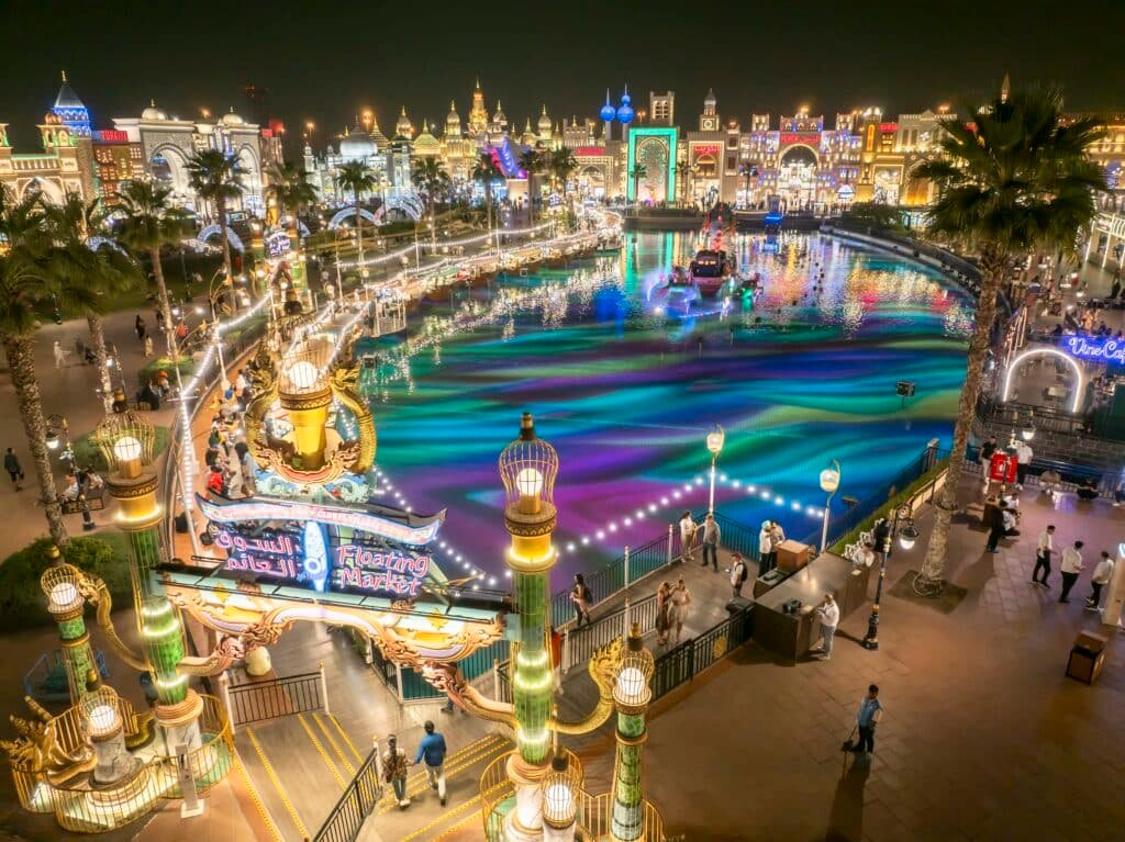 A vibrant nighttime view of an illuminated Global Village Dubai with colourful lights reflecting on the water.