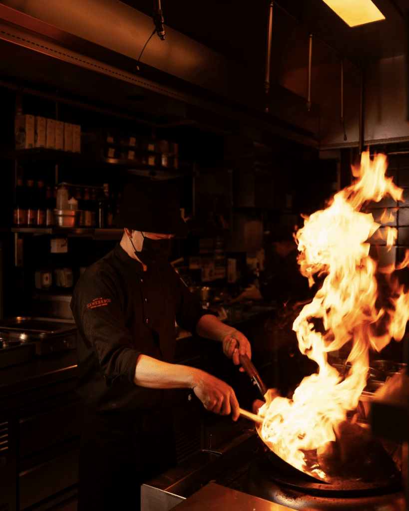 A chef skillfully handles a flaming wok in a dimly lit kitchen.