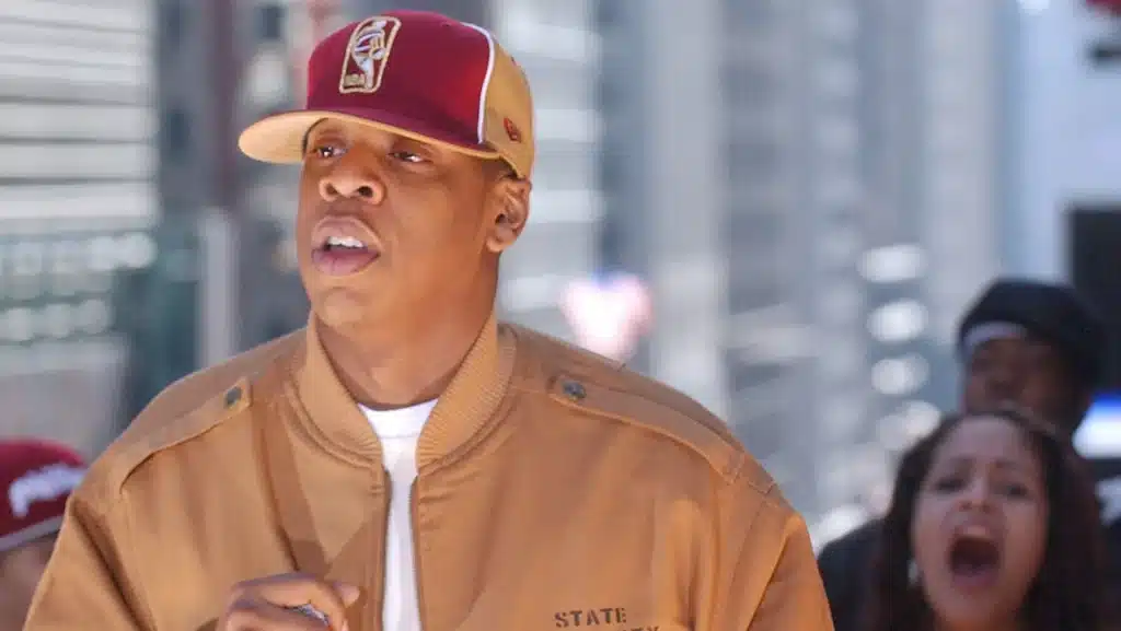 Person wearing a brown jacket and red and gold cap walking in an urban setting.