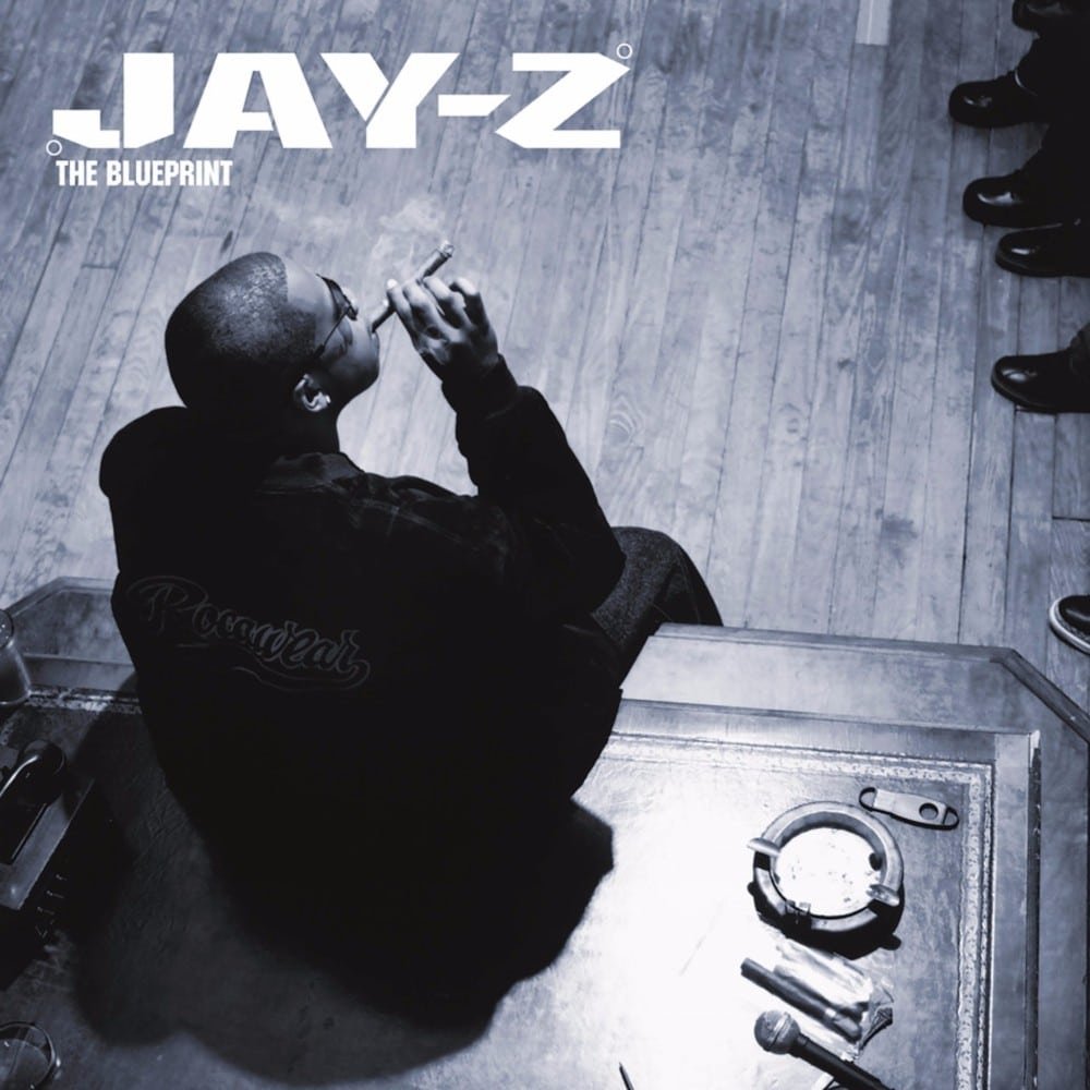 A man seated at a table with a cigar, viewed from above, with "JAY-Z The Blueprint" text in the top left.
