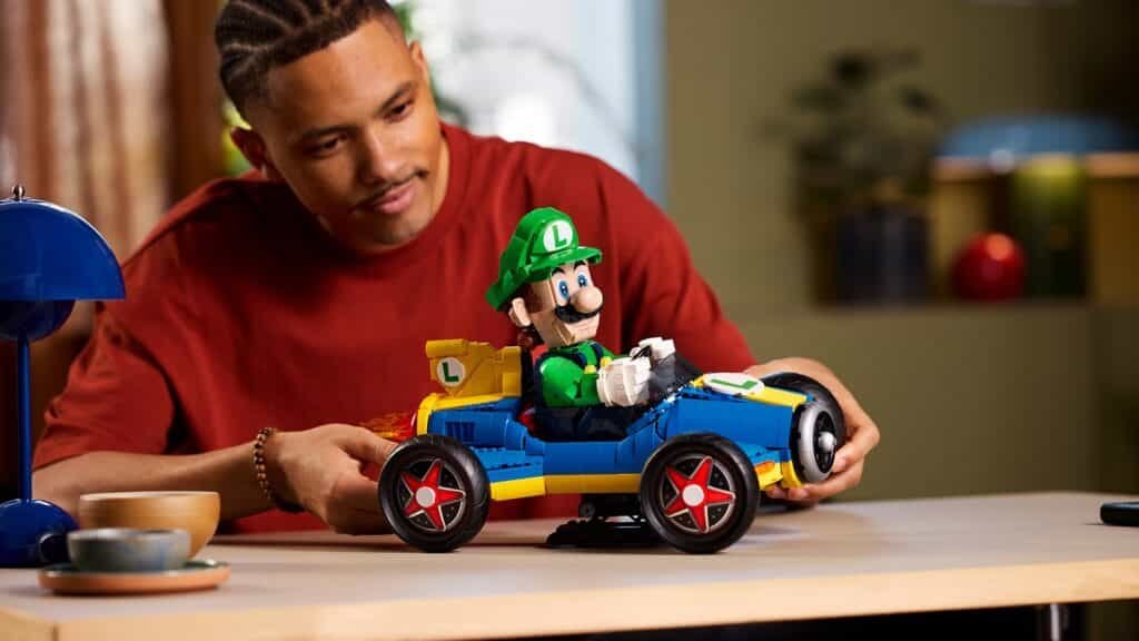 A person assembling a toy go-kart with a Luigi character from a building block set on a table.