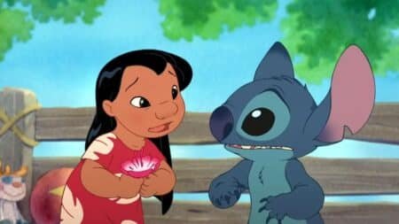 A girl in a red dress holds a flower while standing next to a blue alien creature in a setting with trees and a wooden fence.