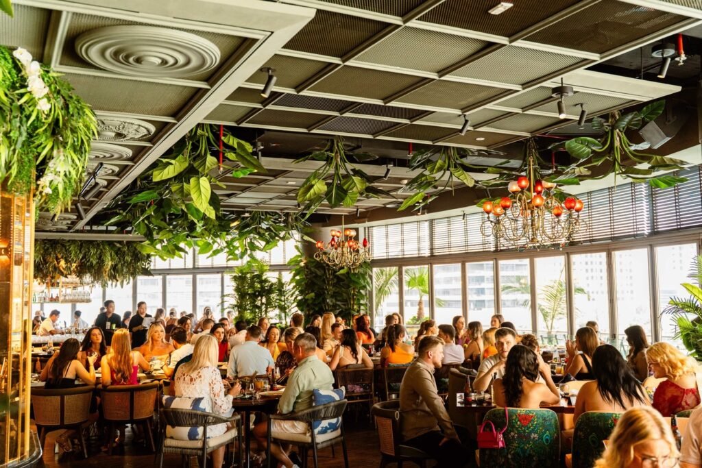 A bustling restaurant filled with people dining under lush green plants and decorative chandeliers.