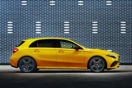 A bright yellow hatchback car parked in front of a patterned brick wall.