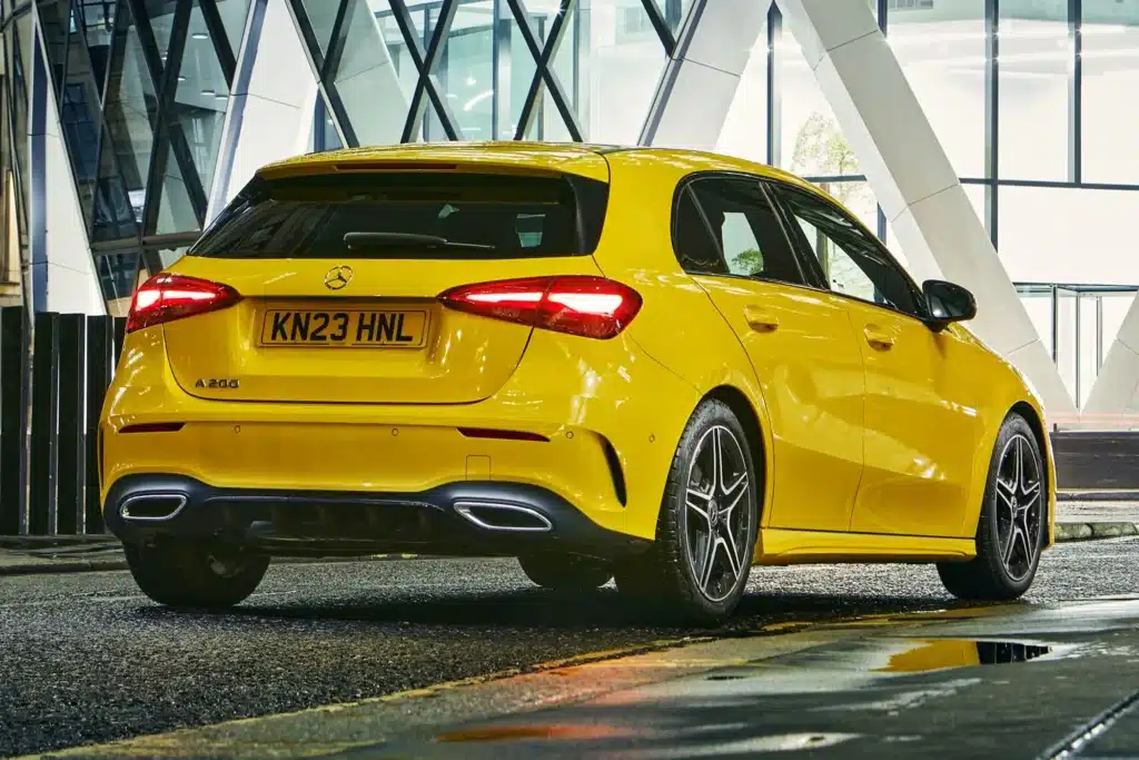 A yellow Mercedes-Benz A-Class car parked on a wet street at night, with modern architecture in the background.