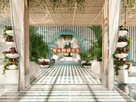 A decorative space with a striped blue and white theme, featuring lush greenery, potted plants, and "Nammos" text on an arched sign.