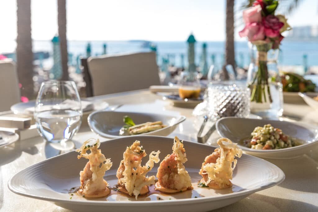 A plate of ornate seafood tempura in Nammos Dubai beachside restaurant setting with a view of the ocean.