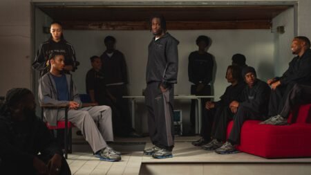 Several people are wearing casual streetwear, with one person standing while others sit on red seating in a dimly lit room.