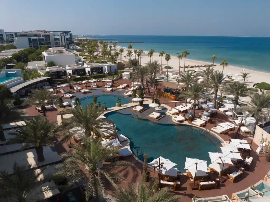 Resort with palm trees, pools, and lounge areas on a beach with a view of the ocean.