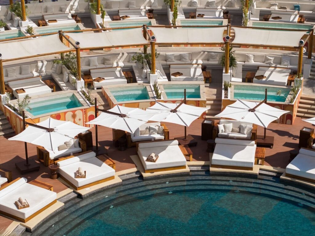 Luxurious poolside area with white sunbeds, large umbrellas, and small plunge pools, surrounding a circular swimming pool.