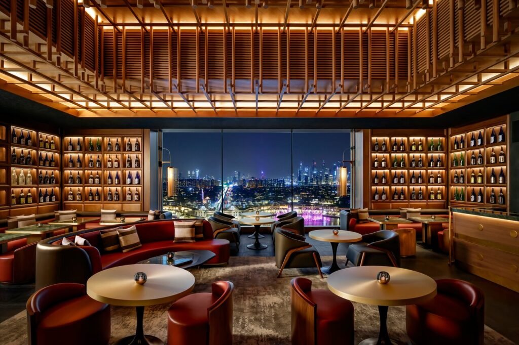 Luxurious rooftop bar with modern red and brown seating, mood lighting, and large windows displaying a cityscape at night.