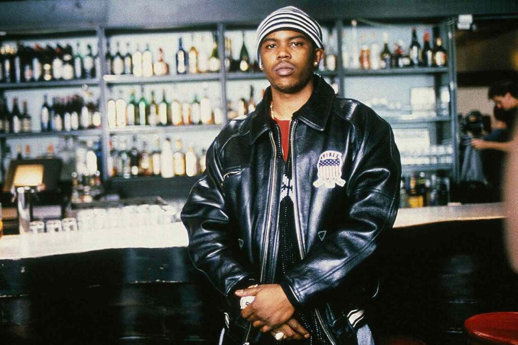 Oliver 'Power' Grant wearing a leather jacket and striped beanie stands in front of a bar stocked with various bottles.