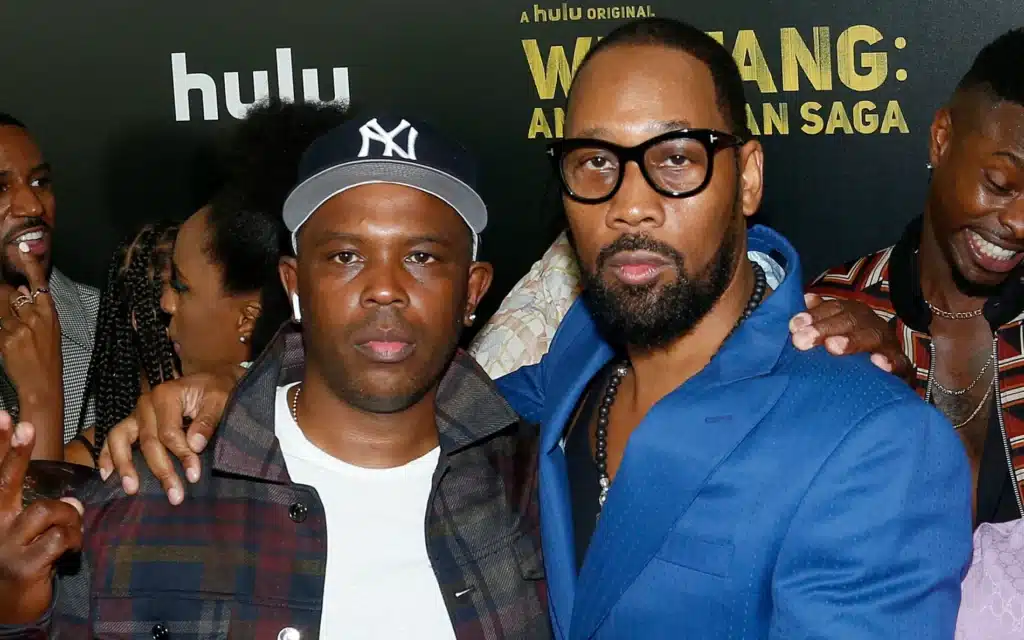 Oliver 'Power' Grant and RZA stand together at an event, with one wearing a cap and the other in a blue blazer. A Hulu banner is in the background.