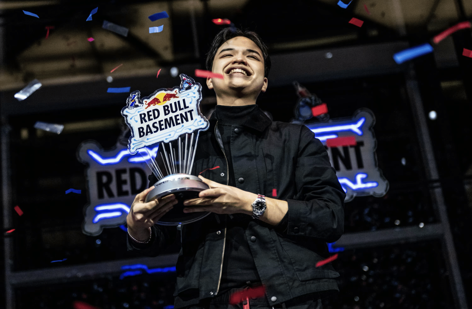 A person holding a Red Bull Basement trophy, smiling, with confetti falling around them.