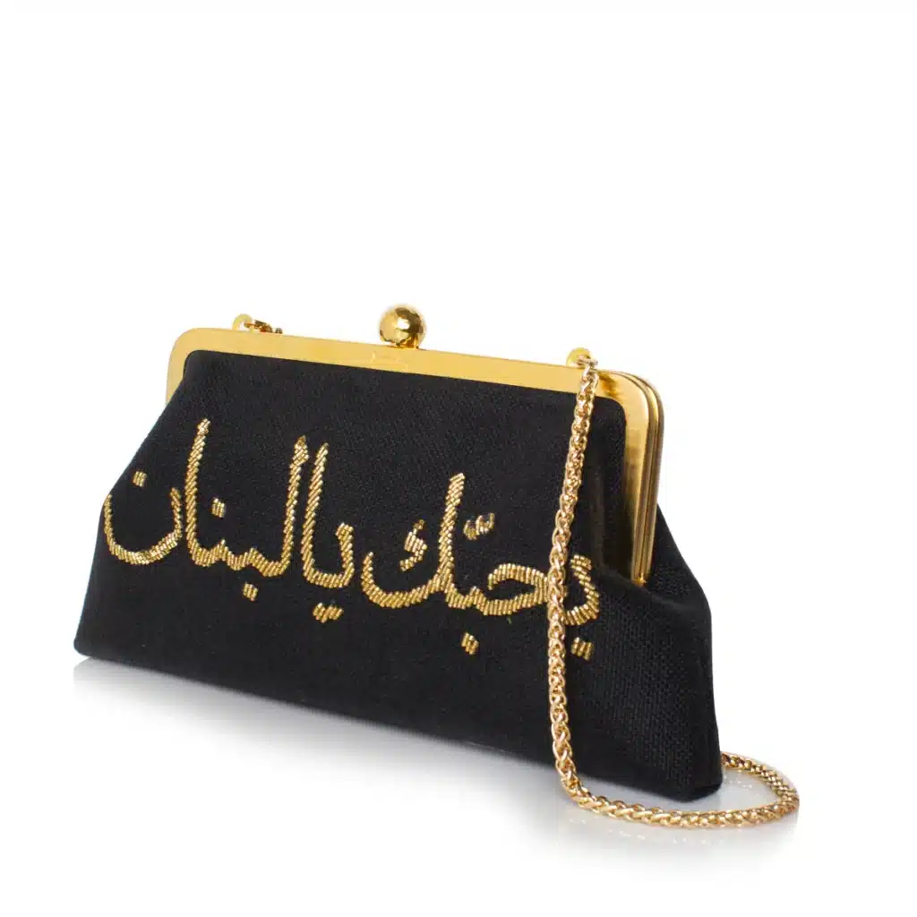 Support Lebanese Brands: Empowering Resilience, Craftsmanship, and Community from the UAE: A black clutch purse with gold Arabic script and a gold chain handle.