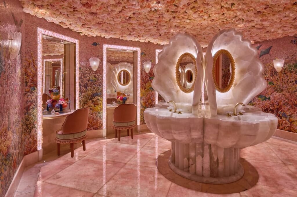Luxurious Sexy Fish Dubai restroom with seashell-shaped sinks, floral ceiling, and coral-themed walls, featuring elegant mirrors and chairs.