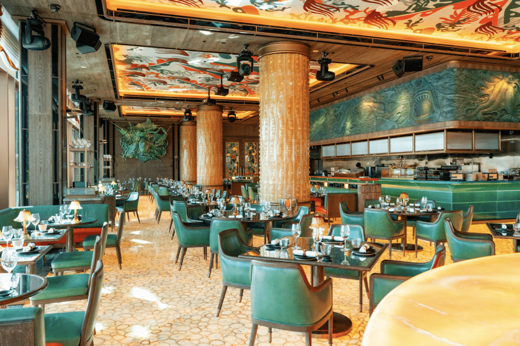 A stylish, modern Sexy Fish Dubai restaurant interior with green chairs, round tables set for dining, decorative columns, and artistic ceiling designs.