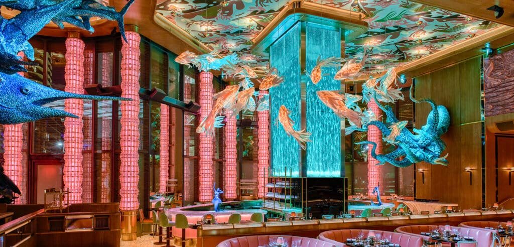 A vibrant restaurant interior featuring marine-themed decor, including colorful fish sculptures, a large octopus, and illuminated columns.