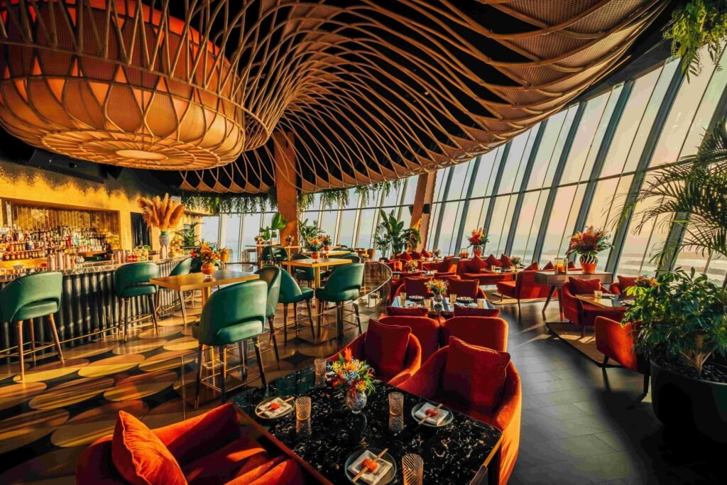 Sushisamba Dubai restaurant with vibrant decor, featuring green and orange seating, a bar with bottles, and large windows offering scenic views.