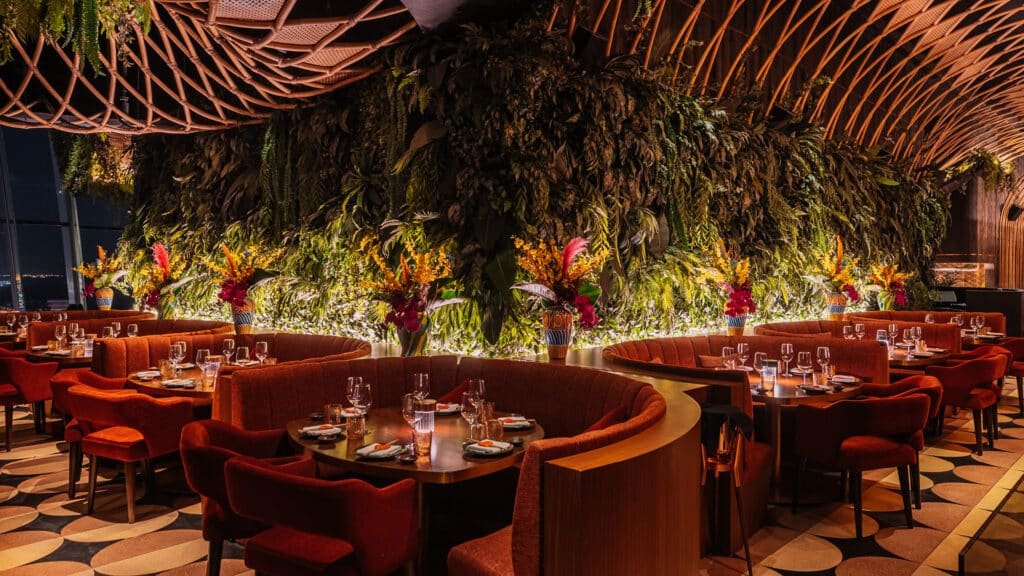 Sushisamba Dubai interior with red seating, circular tables set for dinner, and lush green vertical gardens adorned with colourful flowers.