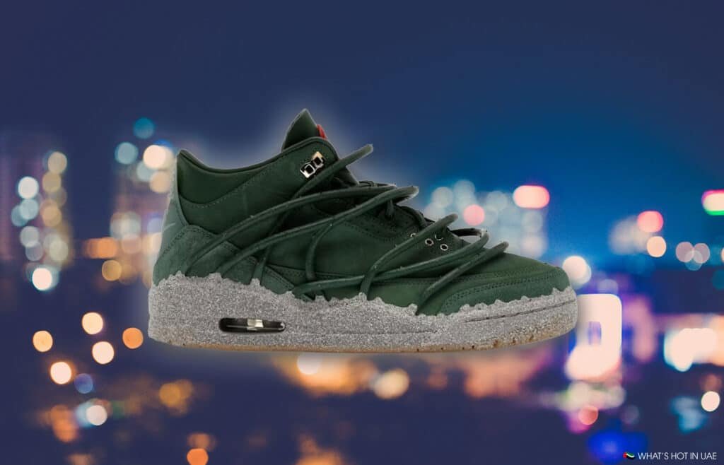 A green high-top sneaker with an intricate lacing design and a speckled gray sole, set against a blurred city lights backdrop.