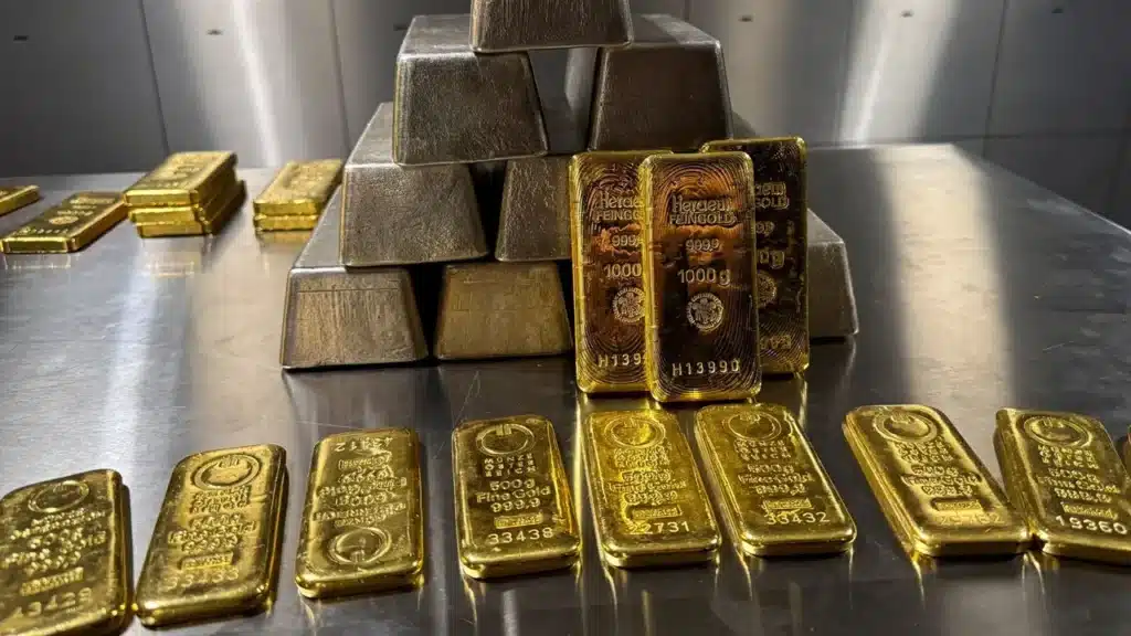 Gold Price Drop: Stacked gold bars and bullion arranged on a reflective surface in an indoor setting.