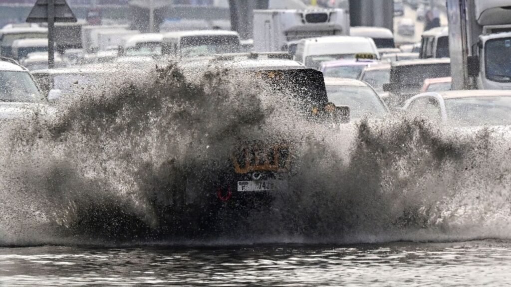 UAE Rain Alert: A vehicle is driving through a large puddle on a congested road, causing a dramatic splash of water.