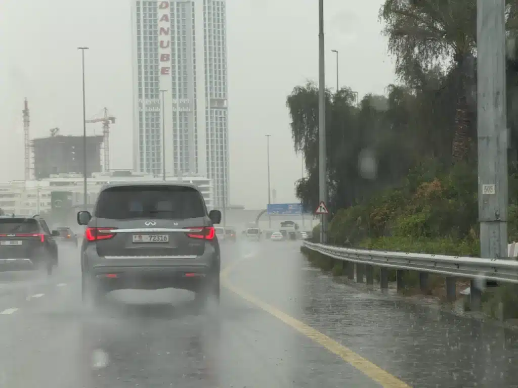 UAE Rain Alert: Cars driving on a rainy highway with high-rise buildings in the background.