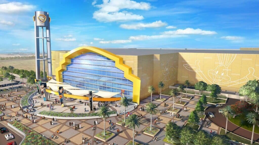 Aerial view of Warner Bros. World Abu Dhabi, featuring a large, yellow-themed entrance and surrounding palm trees with visitors outside.