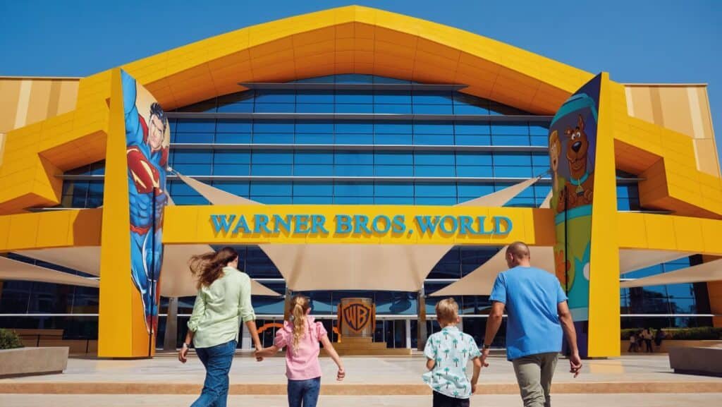 A family walks toward the entrance of Warner Bros. World, with large character images on either side of the building.