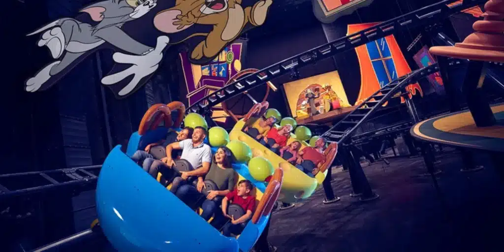 People riding a colorful roller coaster with cartoon character decorations.