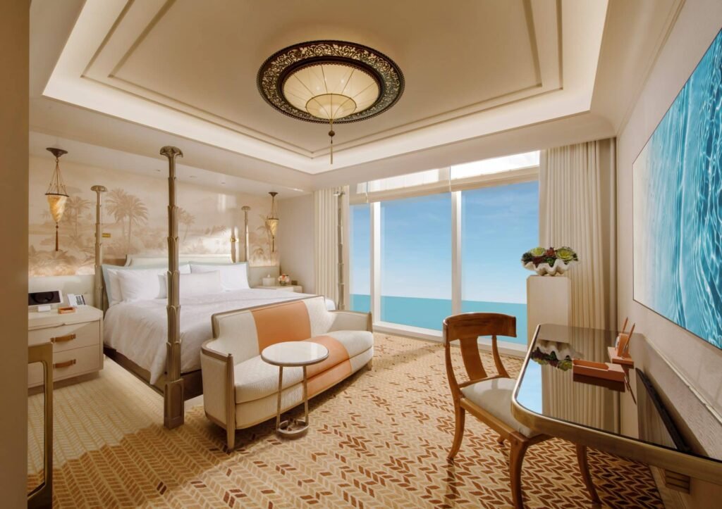 Luxurious hotel room with a large bed, elegant lighting, a cozy seating area, and a window offering an ocean view.