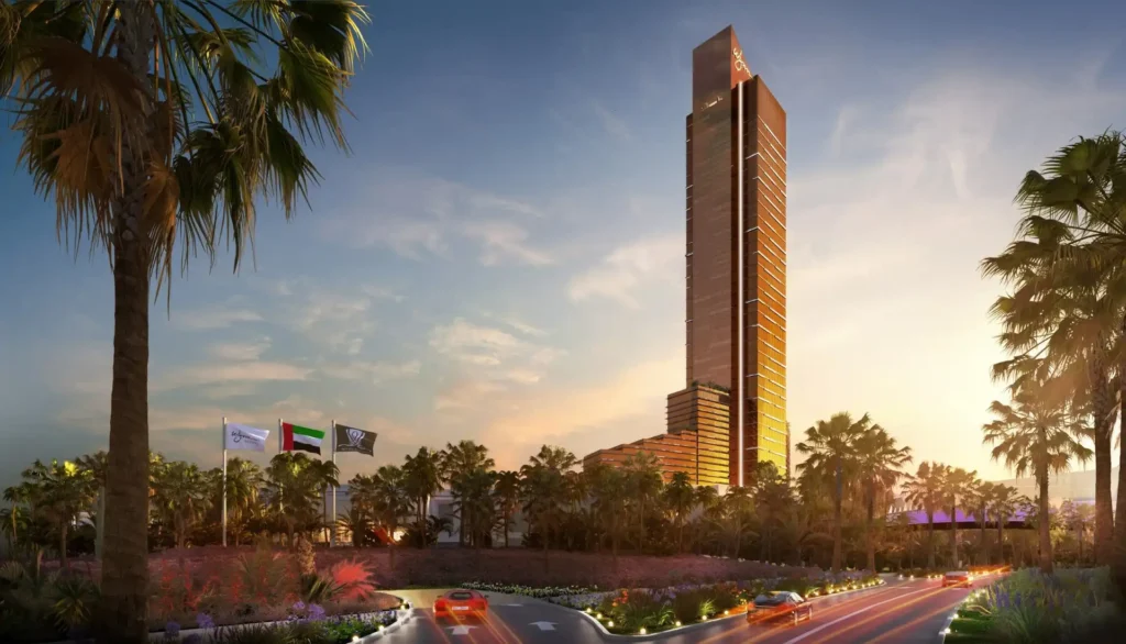 Tall, modern skyscraper with a golden facade surrounded by palm trees, flags, and a busy road at sunset.