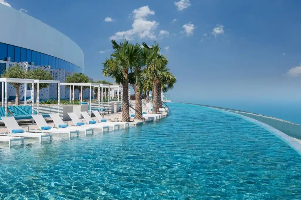 A luxurious curved infinity pool with lounge chairs and palm trees, overlooking a clear blue sky and ocean.