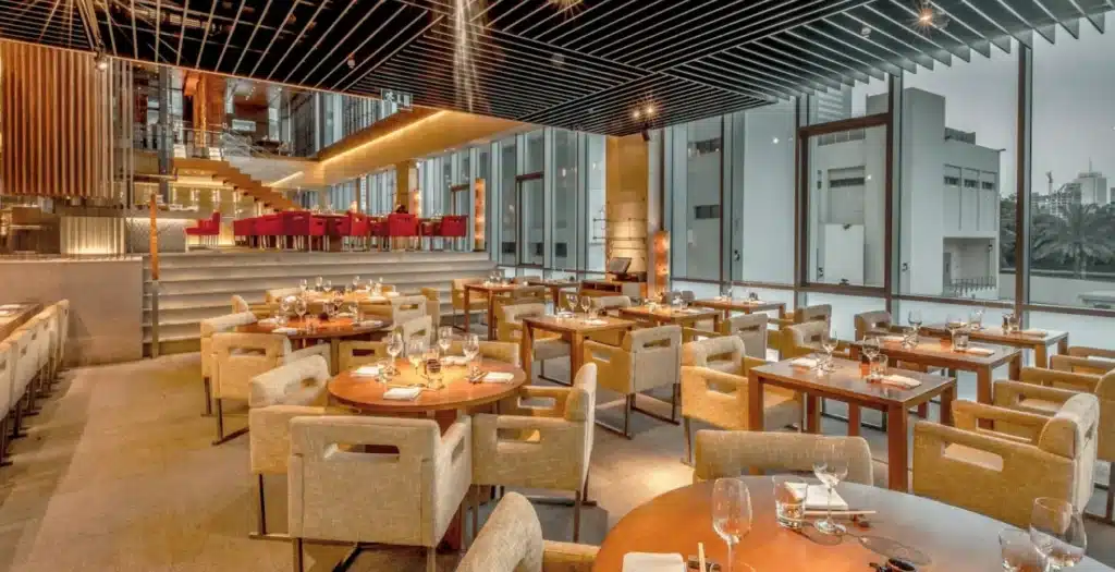 spacious, modern Zuma Dubai DIFC restaurant with wooden tables, beige cushioned chairs, and large windows providing natural light.