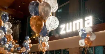 Balloons in blue, gold, and white decorate an indoor space with a bright "zuma" sign on a wall.