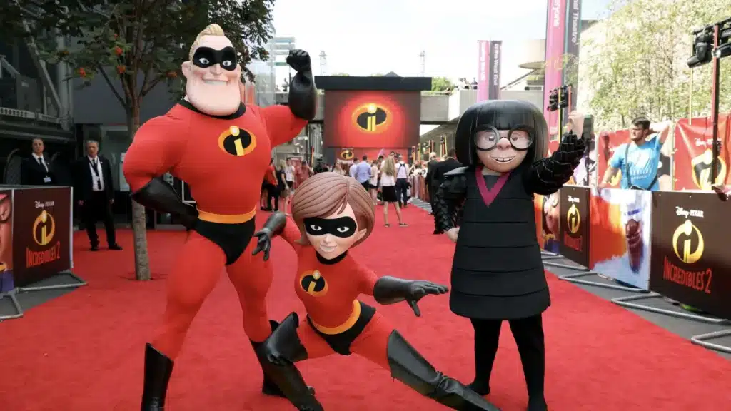 Characters from "The Incredibles" pose on a red carpet, including Mr. Incredible, Elastigirl, and Edna Mode.