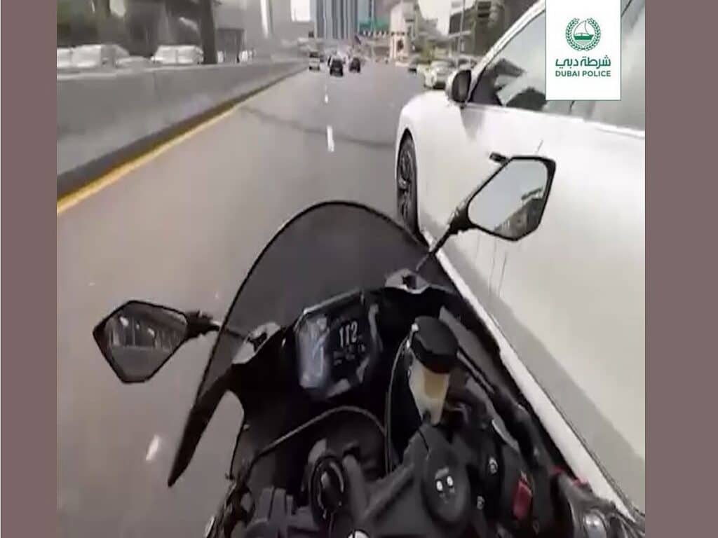 Dubai Police Seize Bikes: Motorcyclist speeding on a highway, closely passing a white car, with a Dubai Police logo visible in the corner.