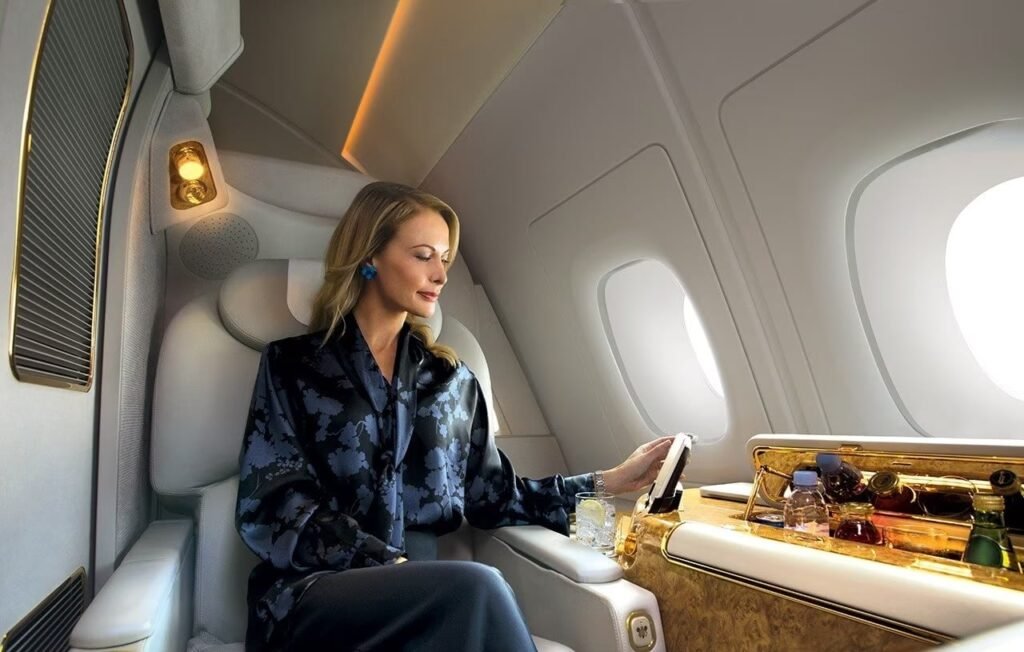 A woman sits comfortably in a luxurious airplane seat, interacting with a device next to a bar with various bottles.
