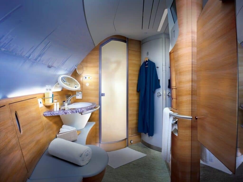 Luxurious Emirates First Class A380 airplane bathroom with wooden accents, elegant sink, and a towel neatly rolled on a bench.