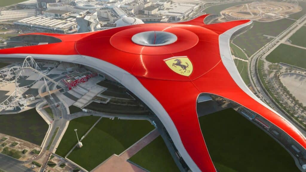 A large, red roof with a Ferrari logo covers Ferrari World Abu Dhabi, featuring futuristic architecture and surrounded by roads.