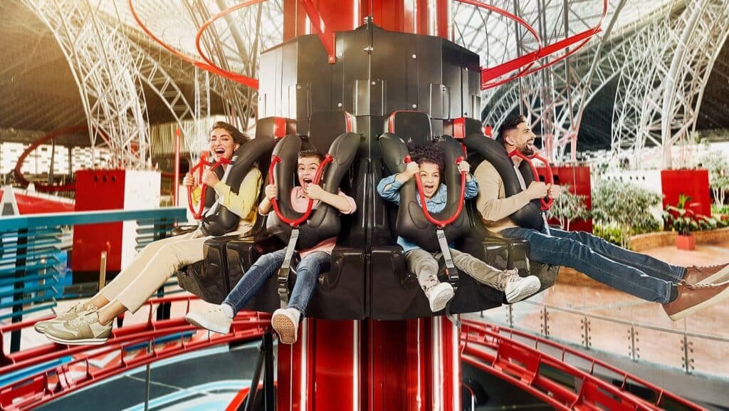 Four people are excitedly riding an Ferrari World Abu Dhabi drop tower ride indoors.