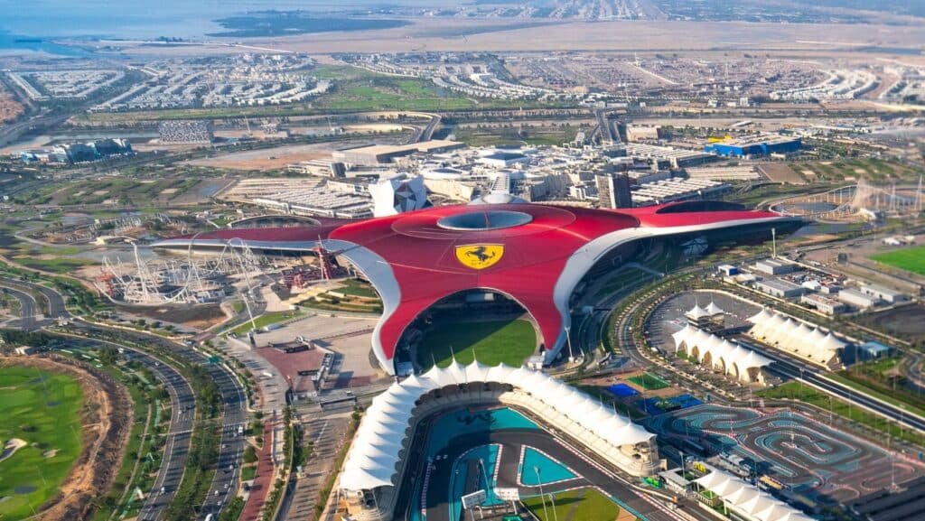An aerial view of Ferrari World Abu Dhabi, showcasing its large red roof with a Ferrari logo and surrounding attractions.