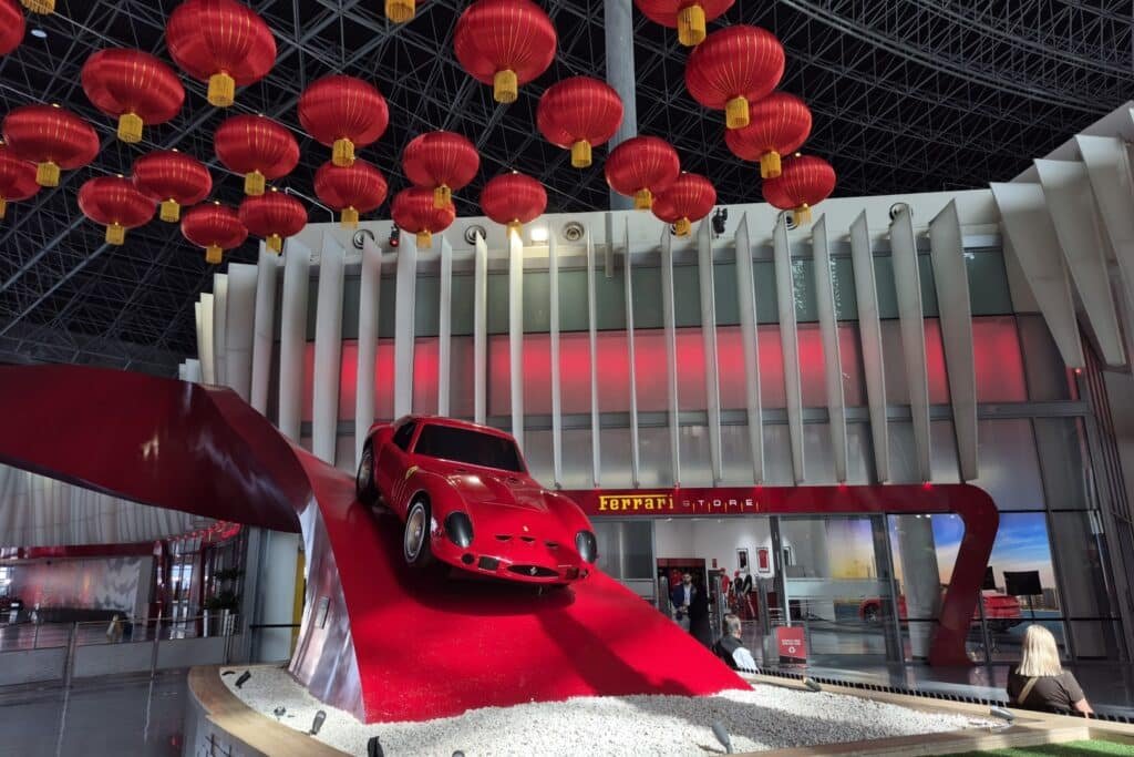 A red sports car is displayed on a tilted platform, surrounded by red lanterns in a modern showroom.