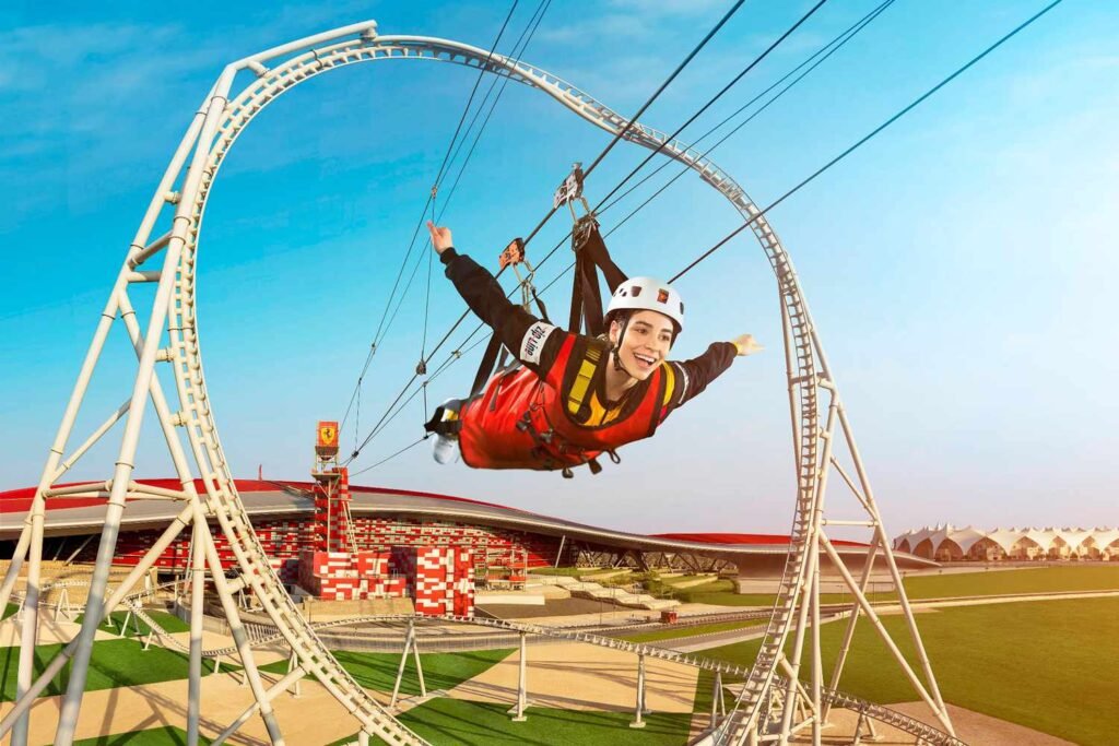 A person in a red jumpsuit and helmet joyfully zip-lining through a large loop against a clear blue sky.