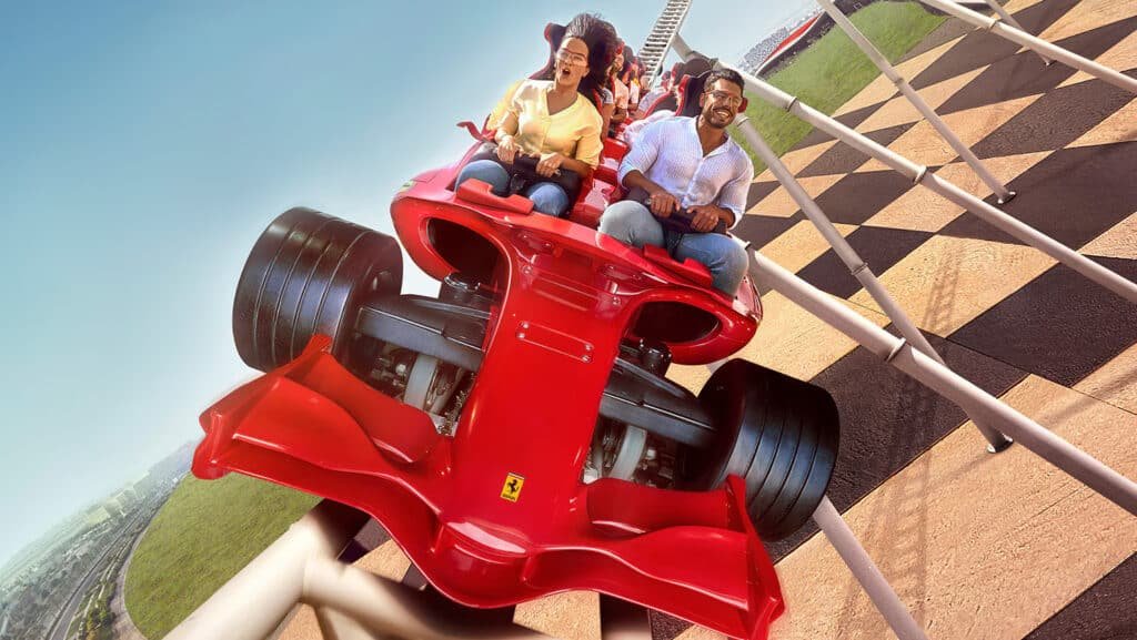People riding a Ferrari-themed roller coaster with excitement, surrounded by track and grassy areas.