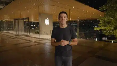 A person stands outside a glass-fronted Apple store at night, wearing a black shirt and watch.